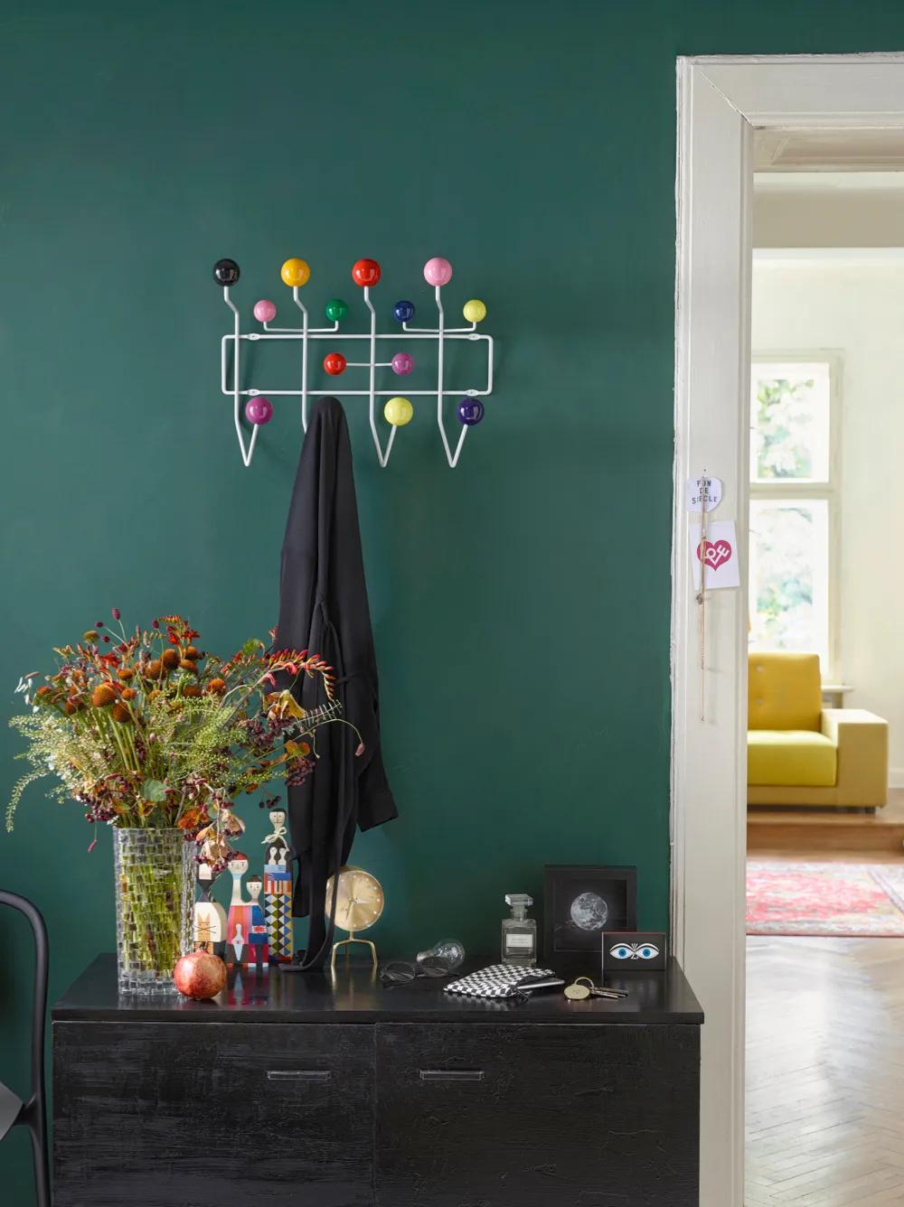 A colourful Eames Hang it all on a bright teal wall beside a bunch of wildflowers