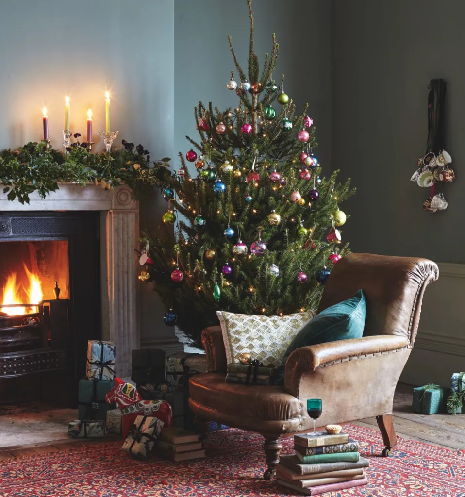 A cosy living room in a Victorian house with a roaring fire and a real Christmas tree laden with colourful antique and vintage baubles.