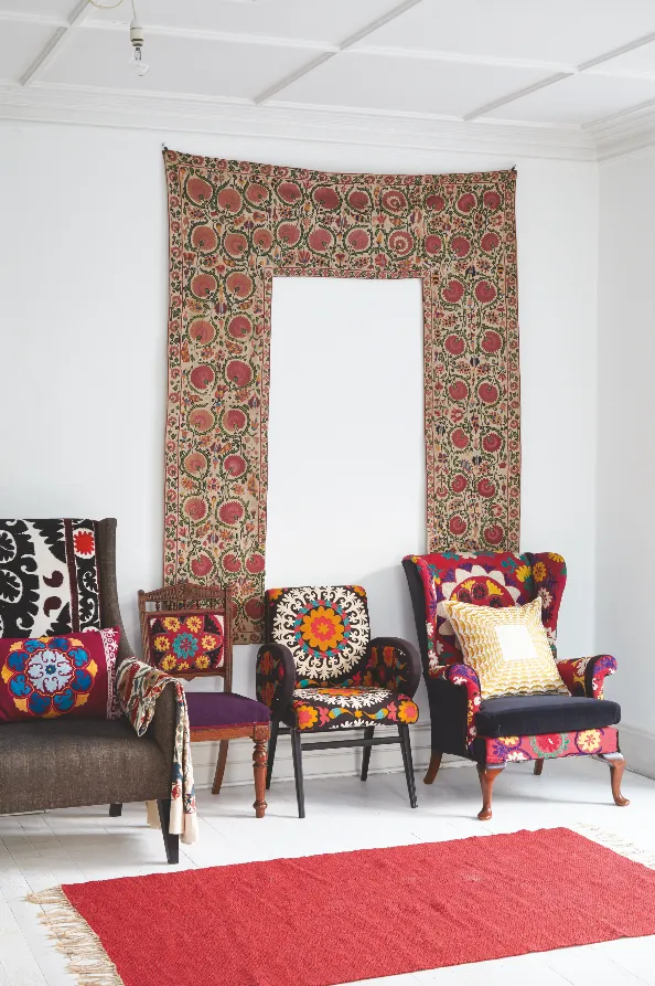 A Partiere suzani hangs on the wall above four vintage armchairs upholstered in vintage Suzani fabric