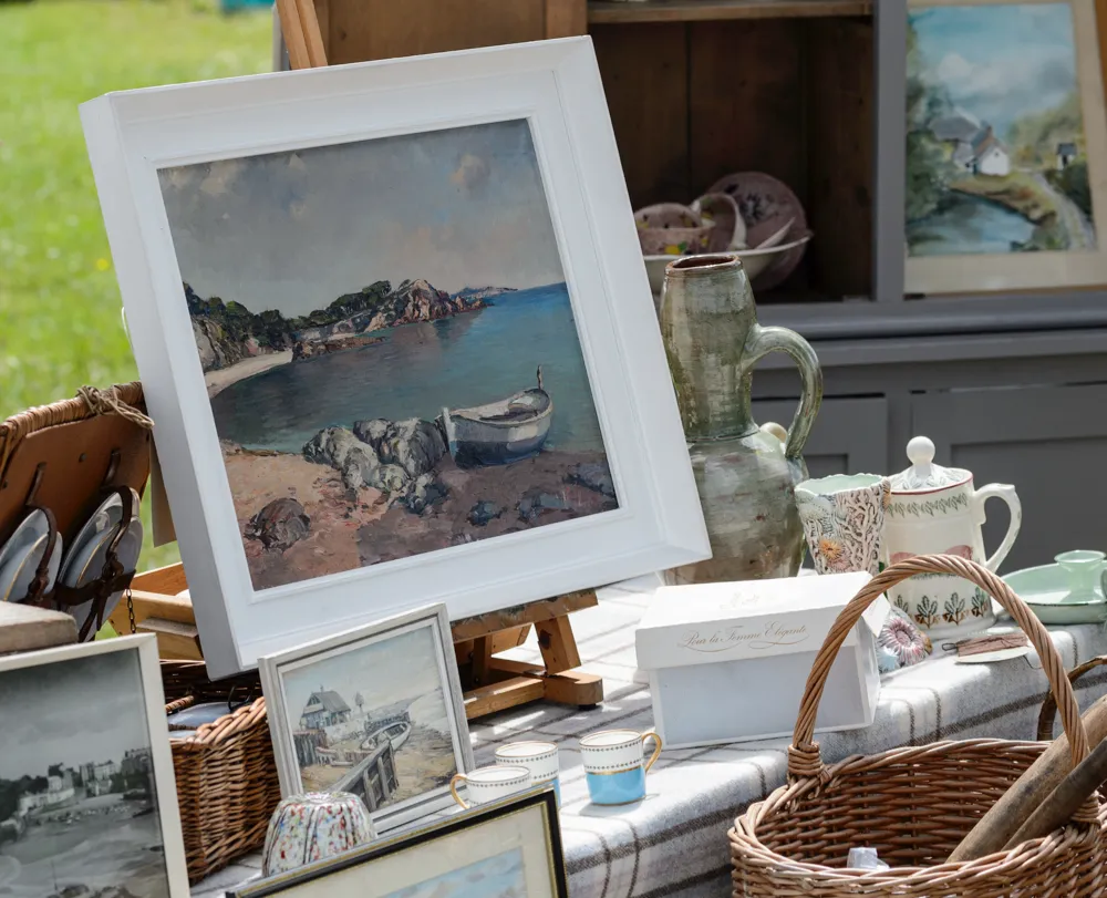 A table laden with antique curios and paintings at an outdoor flea market
