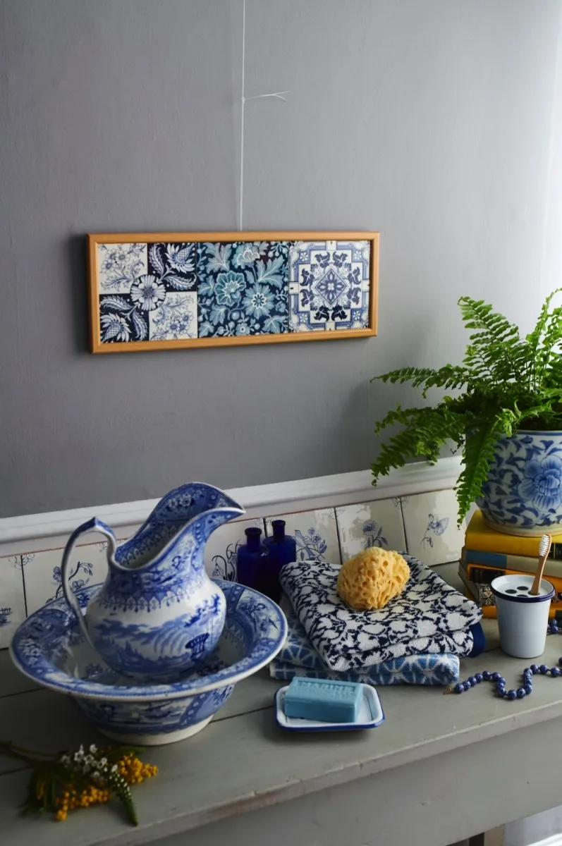 A basin on a mantelpiece below a framed set of English Delft tiles