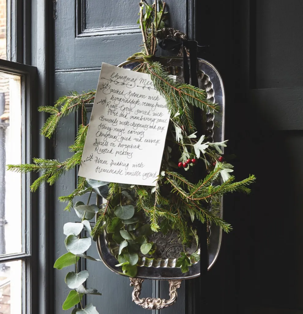A handwritten Christmas dinner menu is tied to an antique silver tray with sprigs of mistletoe and evergreen.