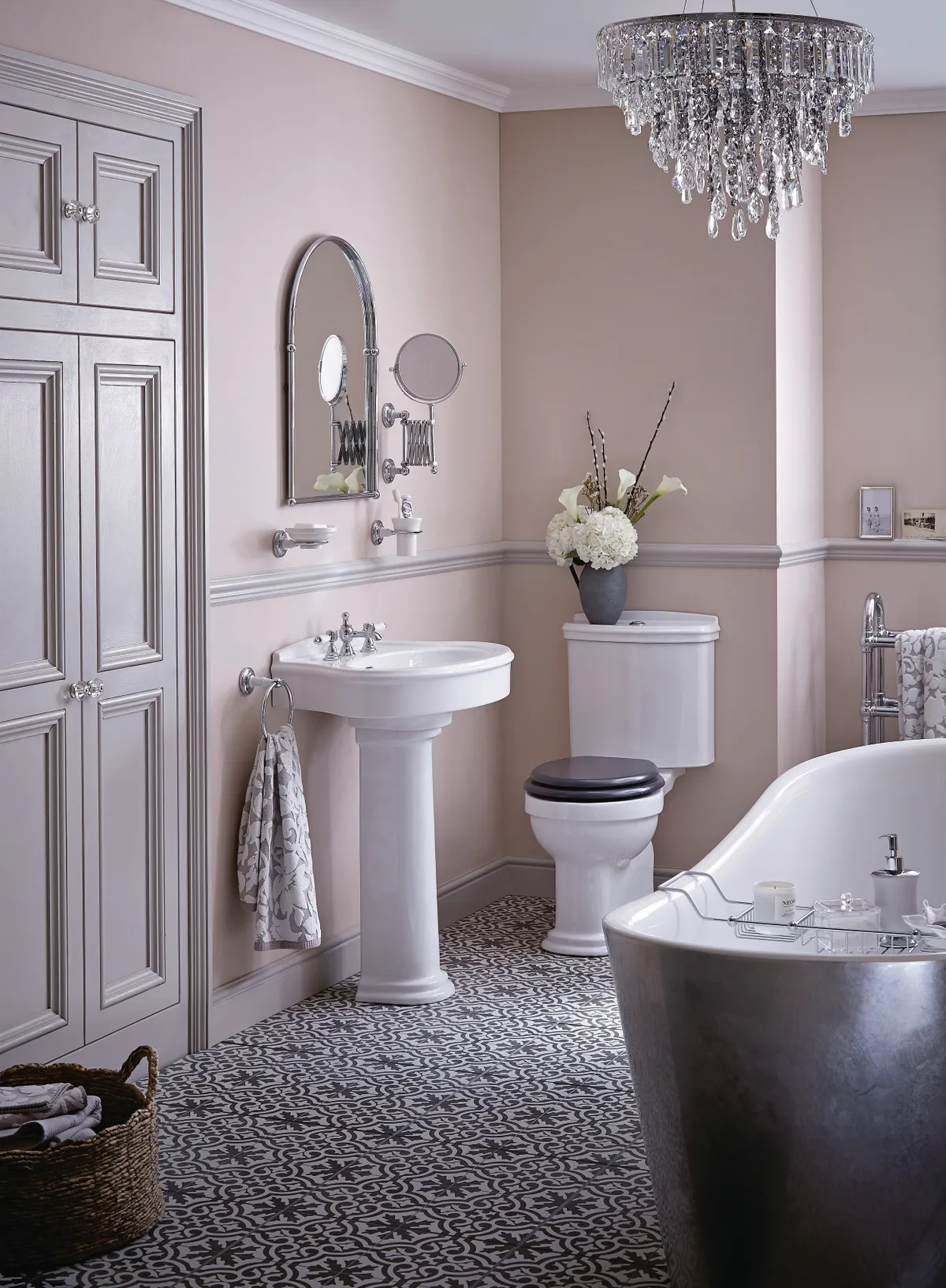 A blush pink bathroom with patterned tiles and a glass chandelier