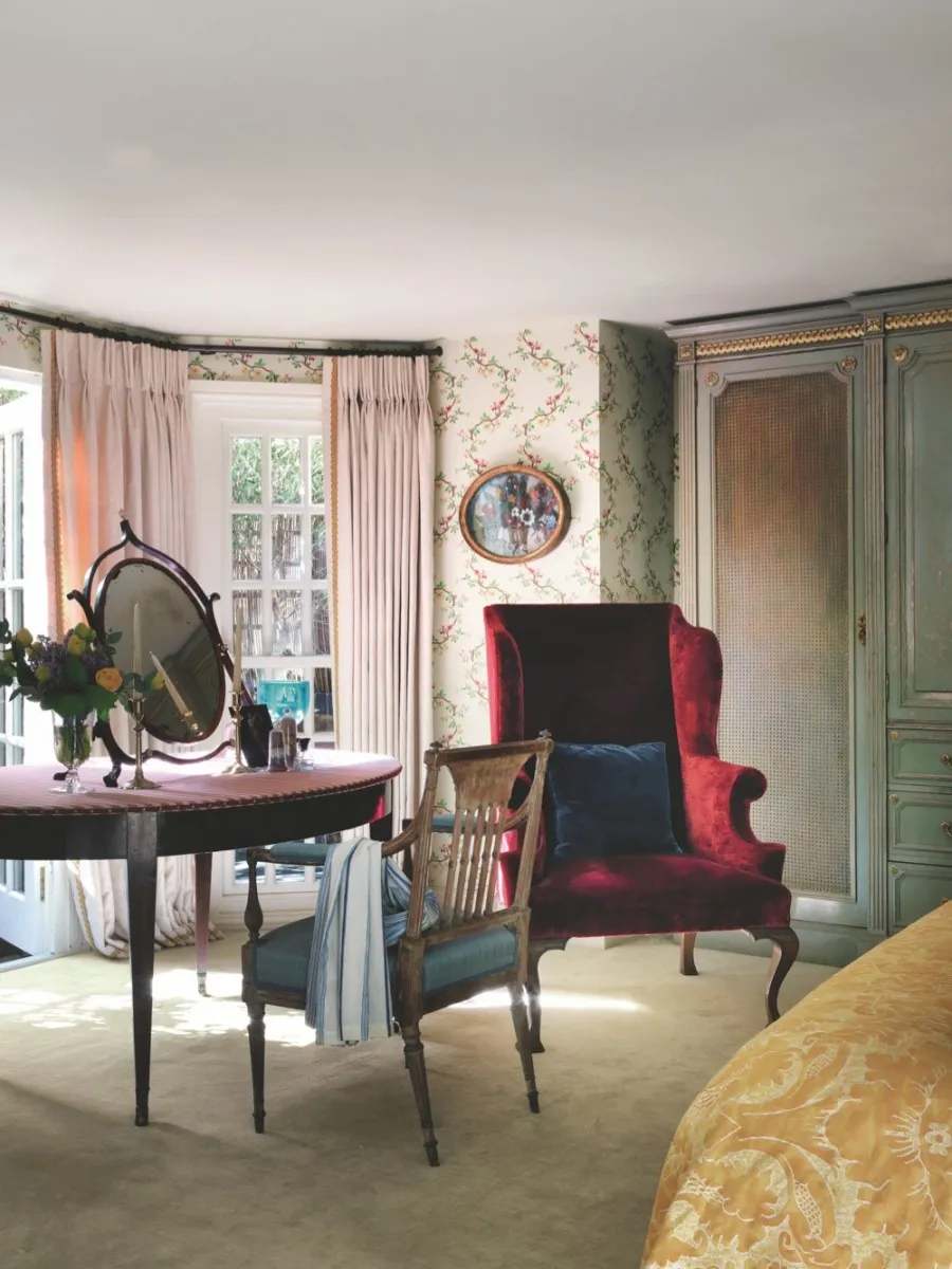 A small bedroom with an antique dressing table, mirror and red velvet armchair