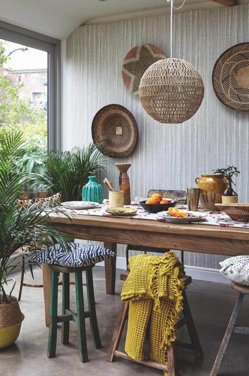 A room with an antique dining table and woven straw baskets on the wall