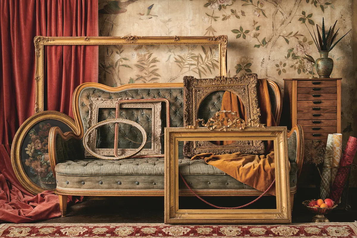 Antique gilded frames in different sizes and shapes leant against an antique sofa.