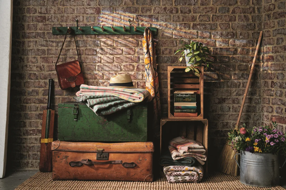 An exposed brick hallway with hooks and antique trunks used to store winter coats and blankets