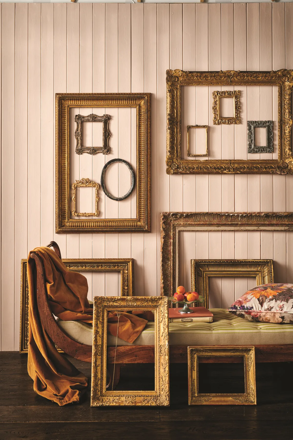Small antique frames displayed in clusters on a pale pink panelled wall