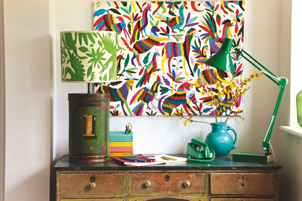 A colourful hand-embroidered artwork above a vintage storage unit with a green anglepoise lamp