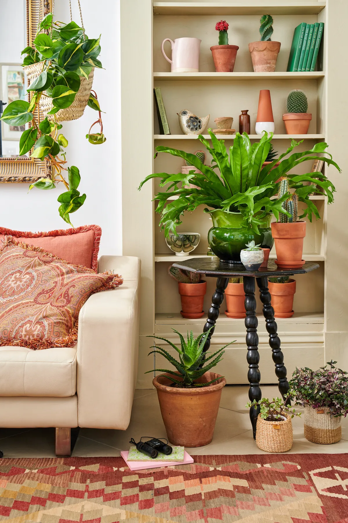 An antique side table laden with leafy plants alongside a contemporary cream sofa.