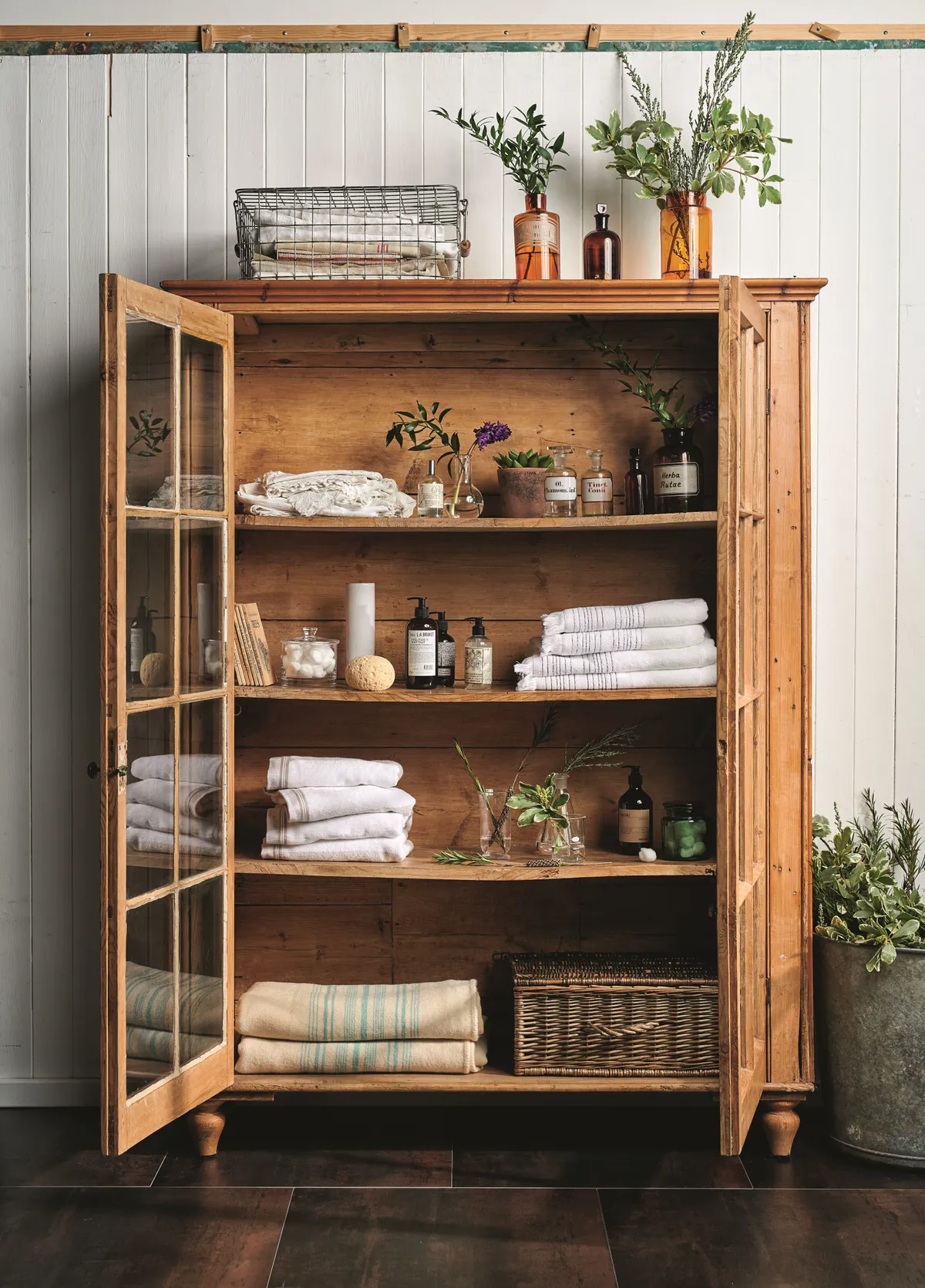 A glass-doored vintage display cabinet is used to show off towels, toiletries and plants in a bathroom.