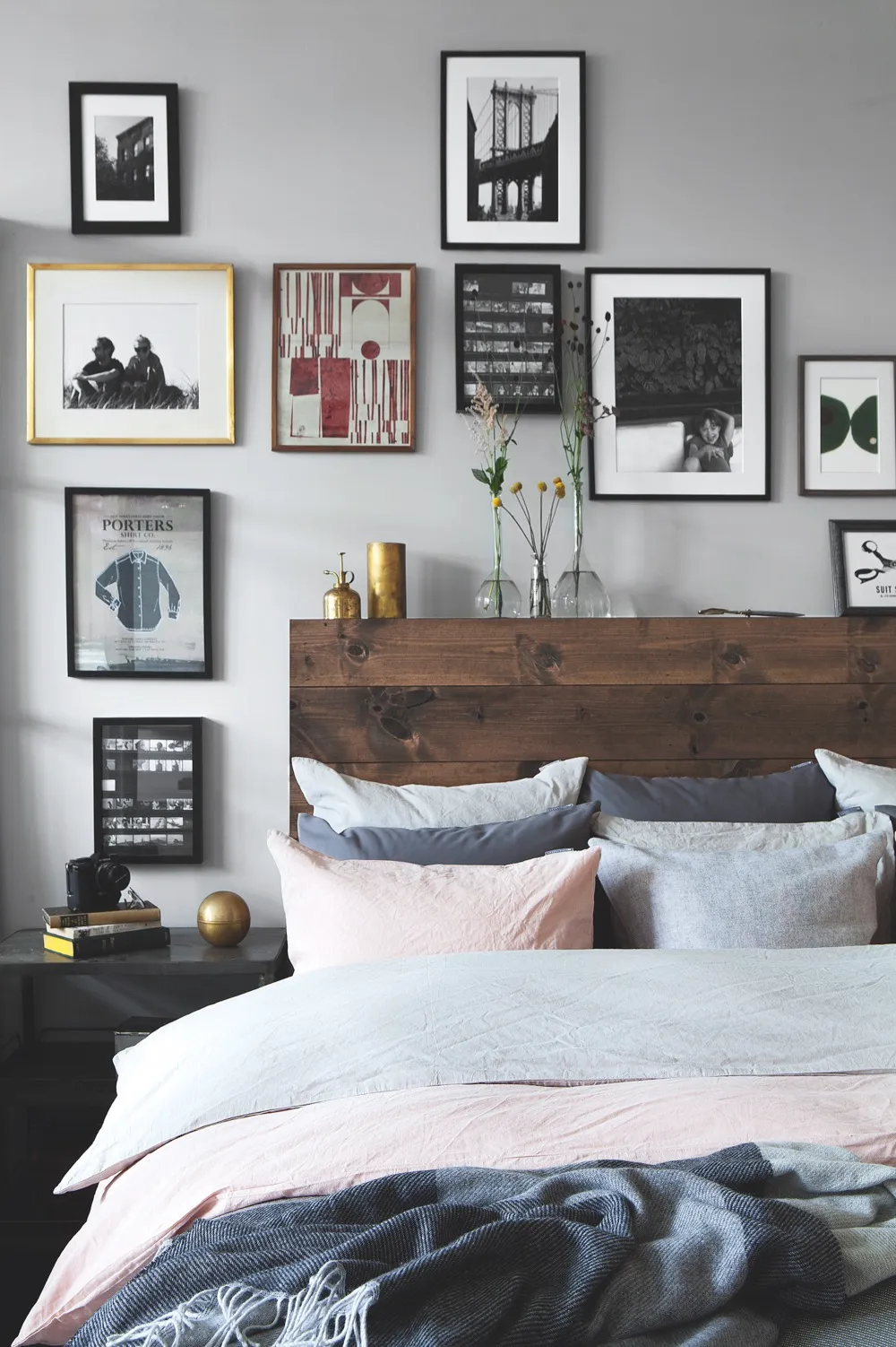 A gallery wall of prints and photographs hanging above a double bed with a rustic wooden headboard