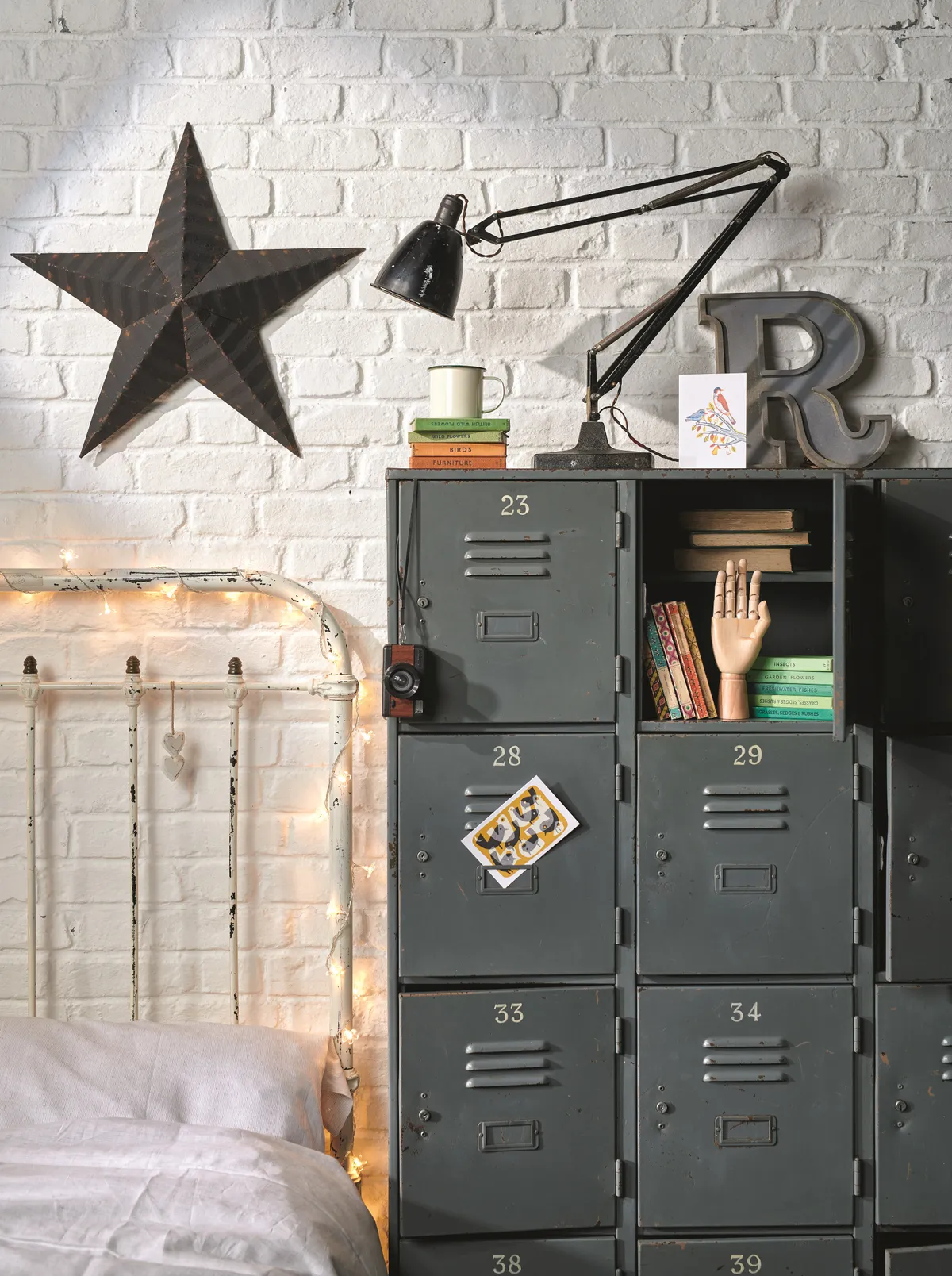 A grey vintage metal locker is used as a bedside table to a distressed metal bed.