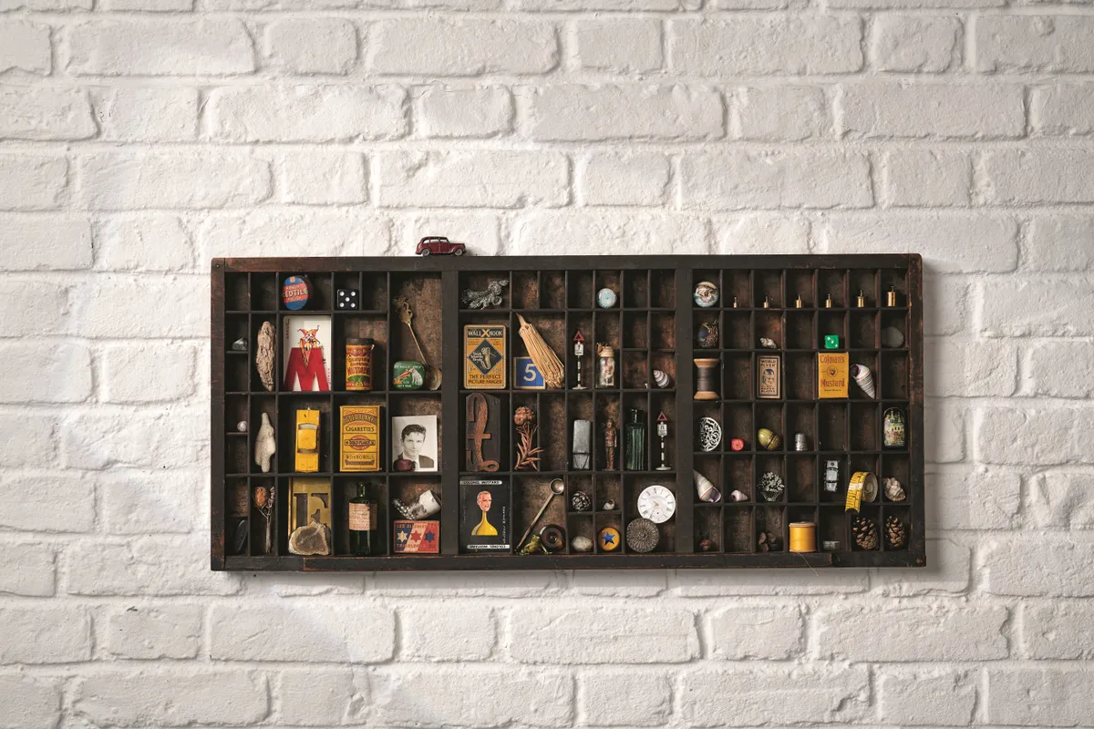 An antique printers tray is mounted on the wall and used to display a collection of small curios