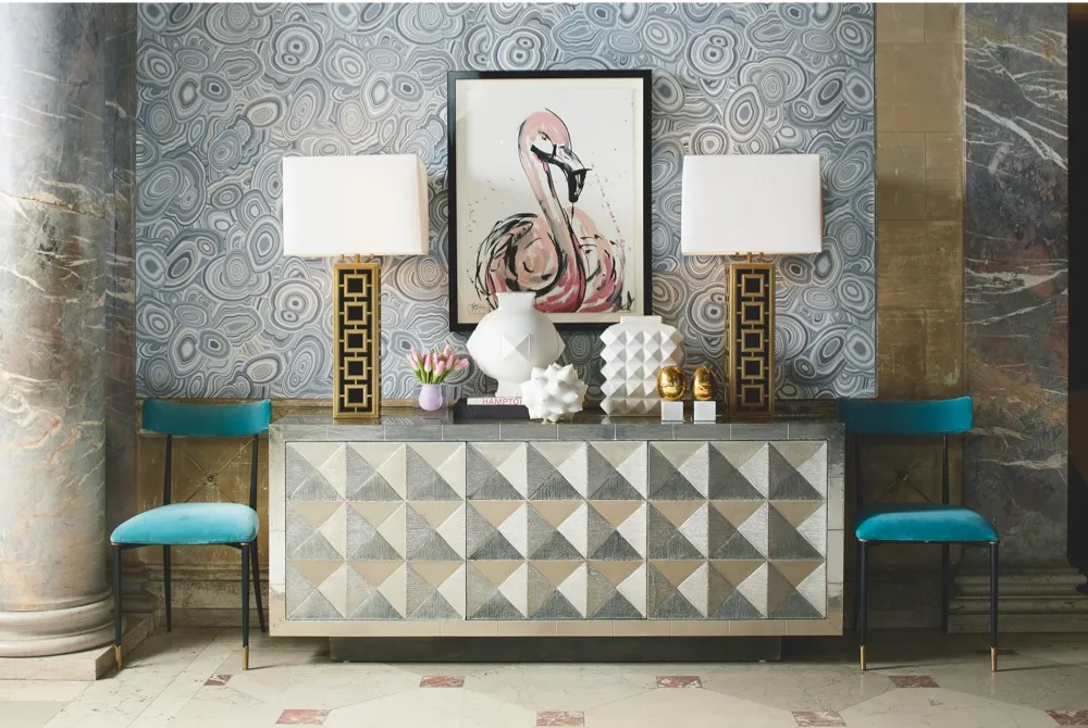 A bold geometric sideboard flanked with blue velvet dining chairs and gold table lamps. A sketch if a flamingo is in the centre.
