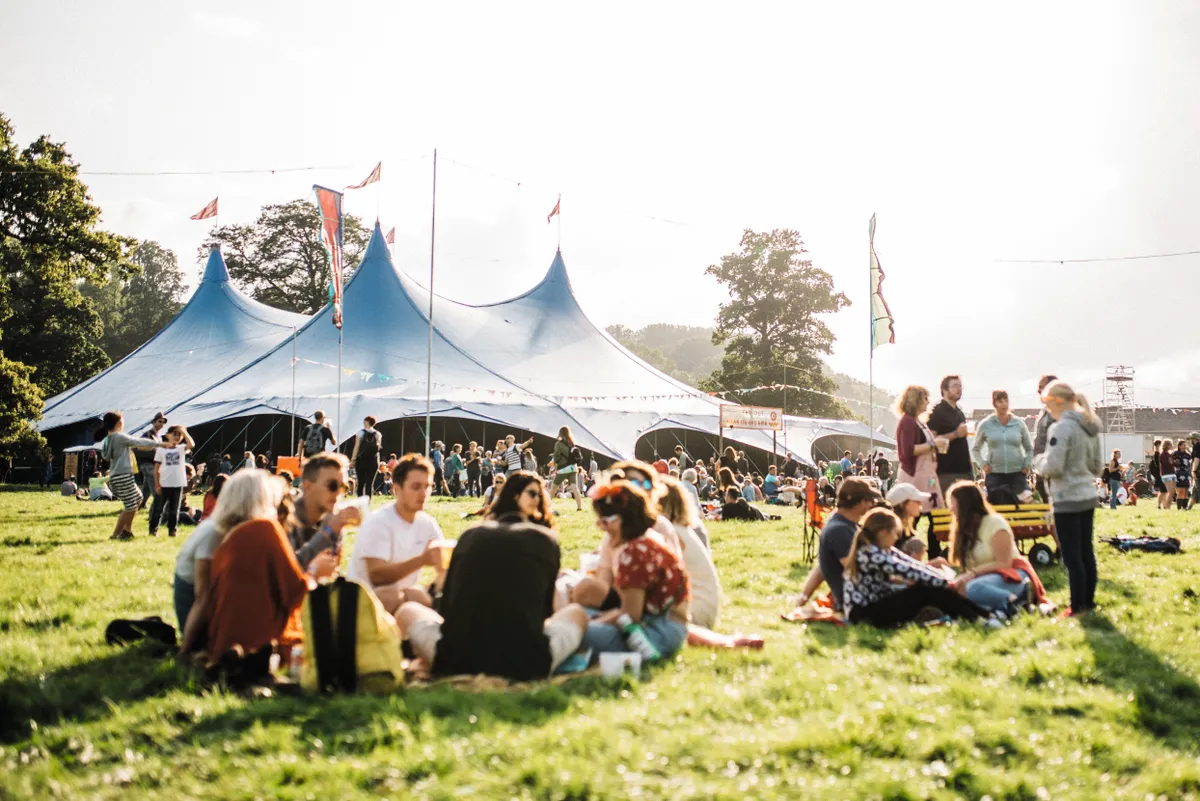 Groups of festival-goers sit under large tents in the sunshine at Green Man 2017