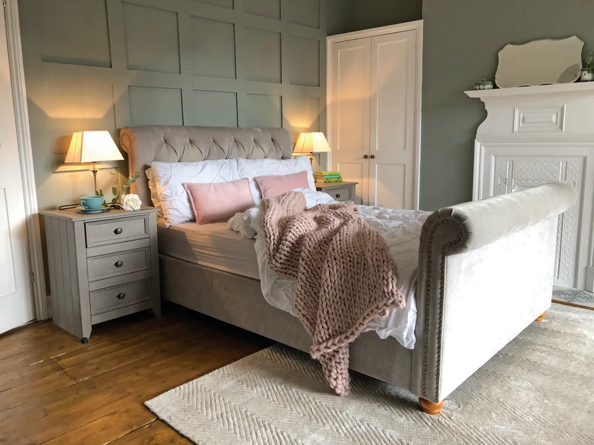 A blush pink bed against a panelled sage green wall