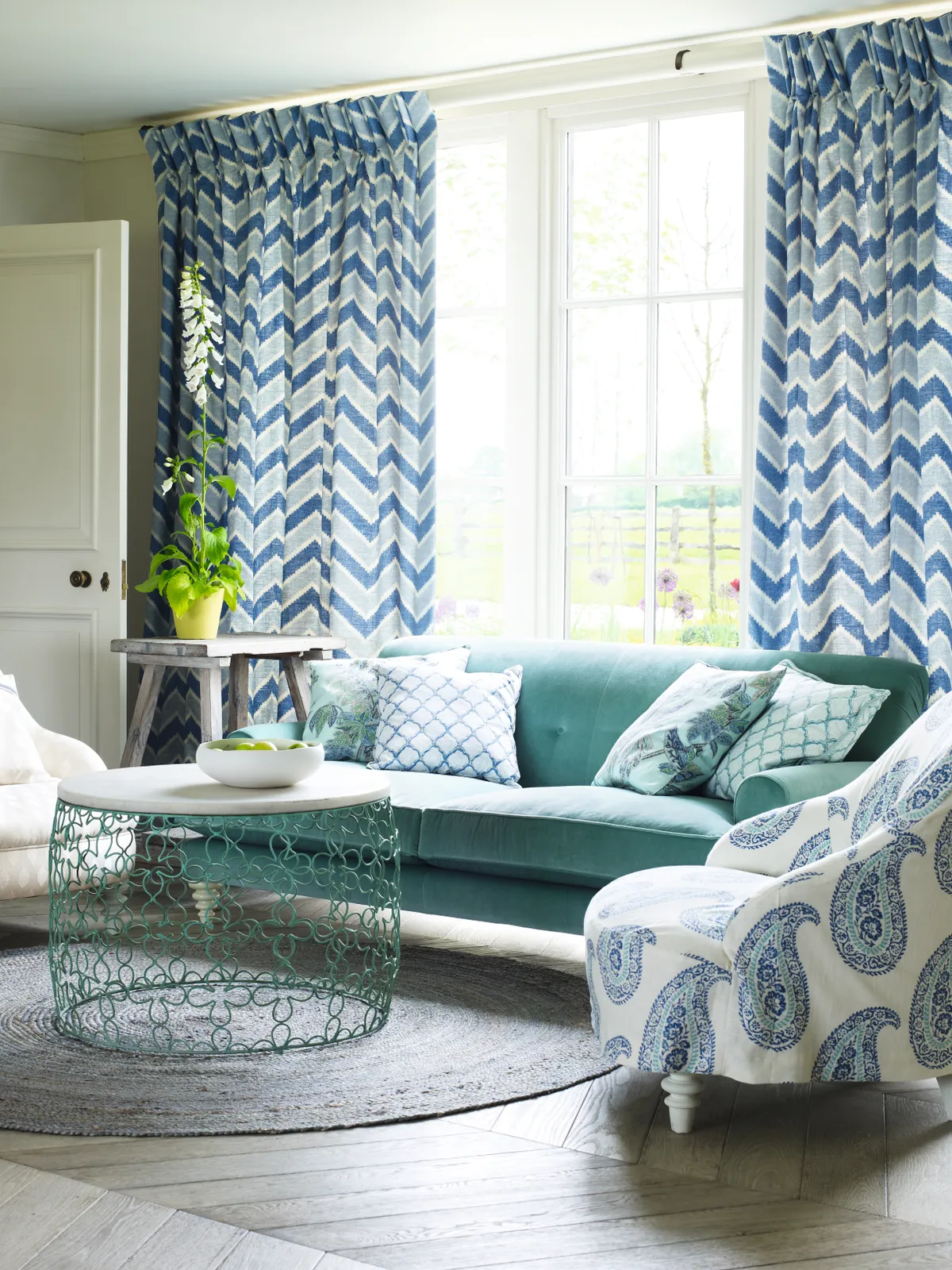 A teal velvet sofa infront of zigzag print blue curtains
