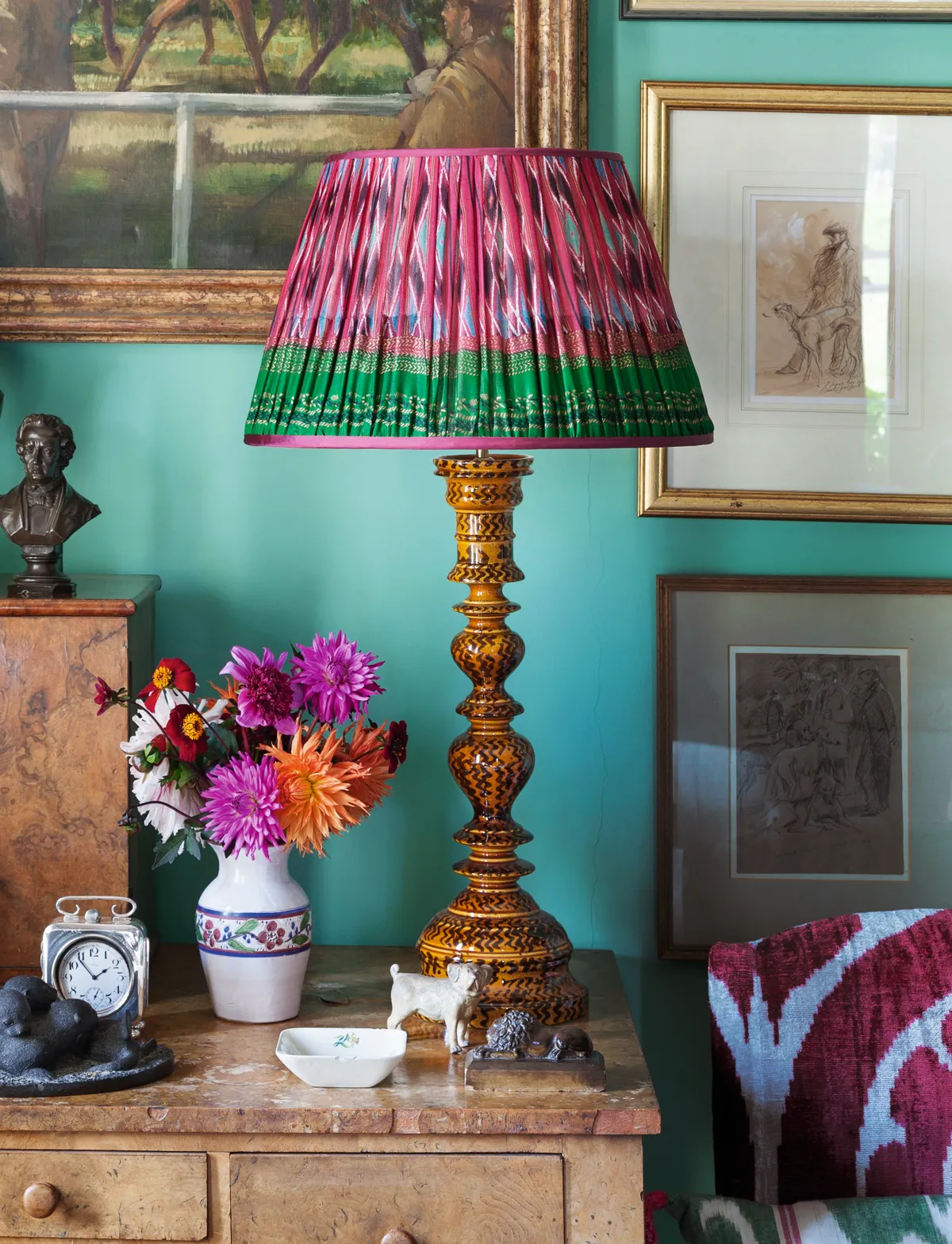 A ruched lampshade on a wooden table lamp against a teal coloured wall