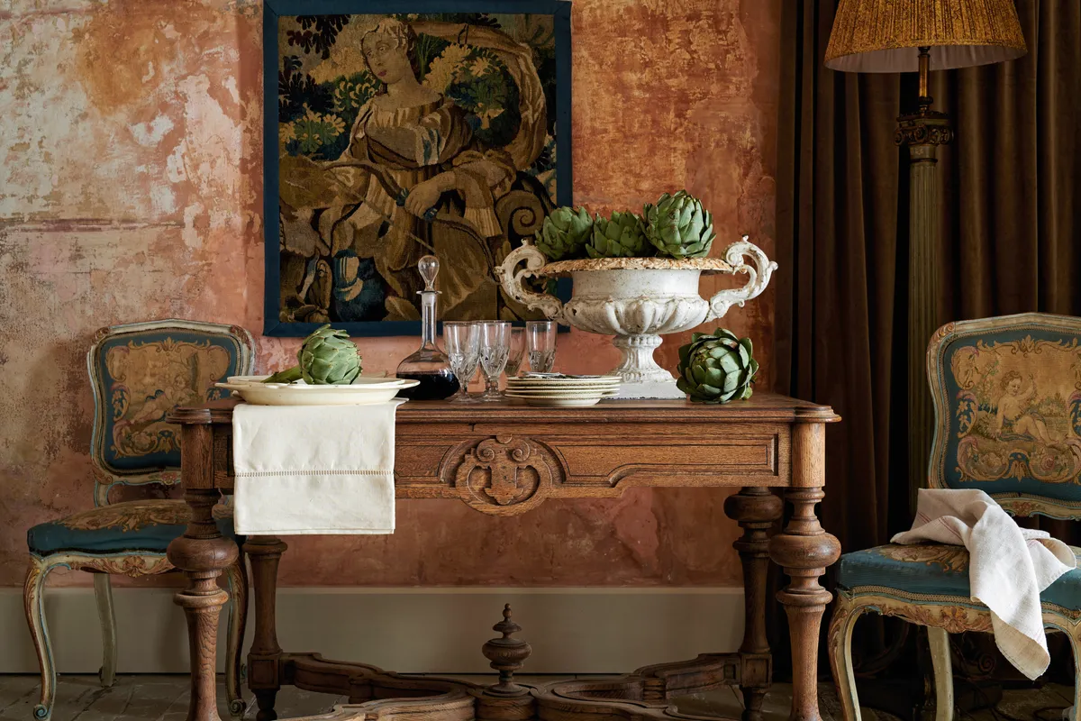 A carved serving table topped with a stone urn of artichokes and heavy glassware.