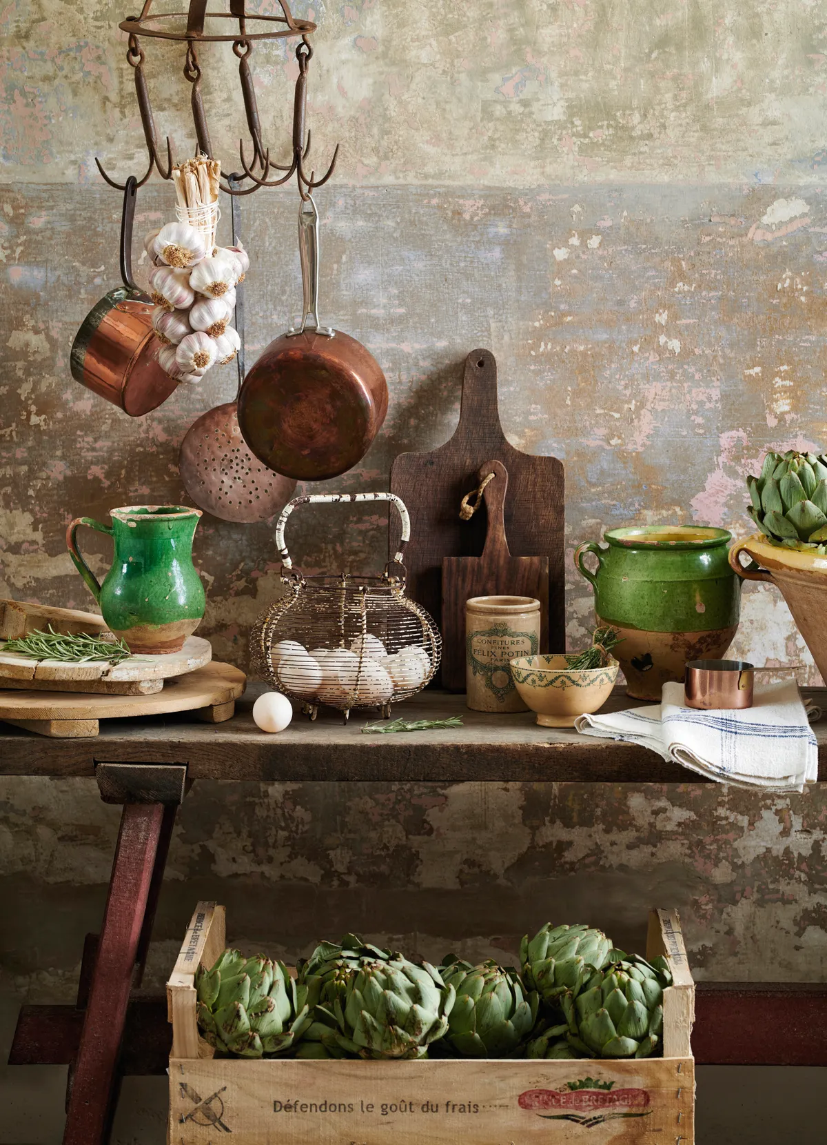 A rustic table topped with confit pots, Confit pots in bright green or yellow glazes, linen tablecloths, plenty of rustic wooden boards and strings of garlic
