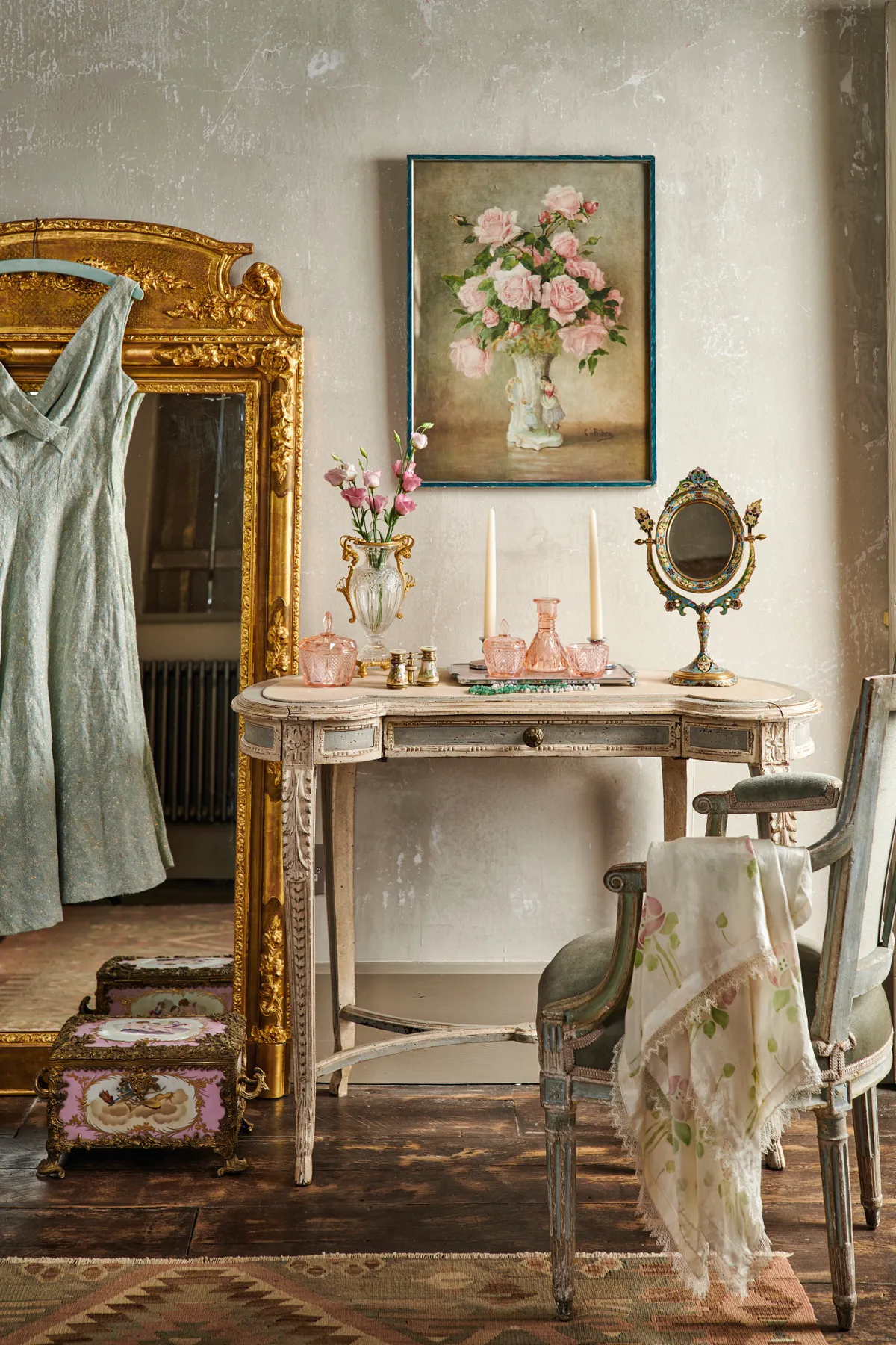 A romantic dressing table topped with pink glassware and a gilt hand mirror.
