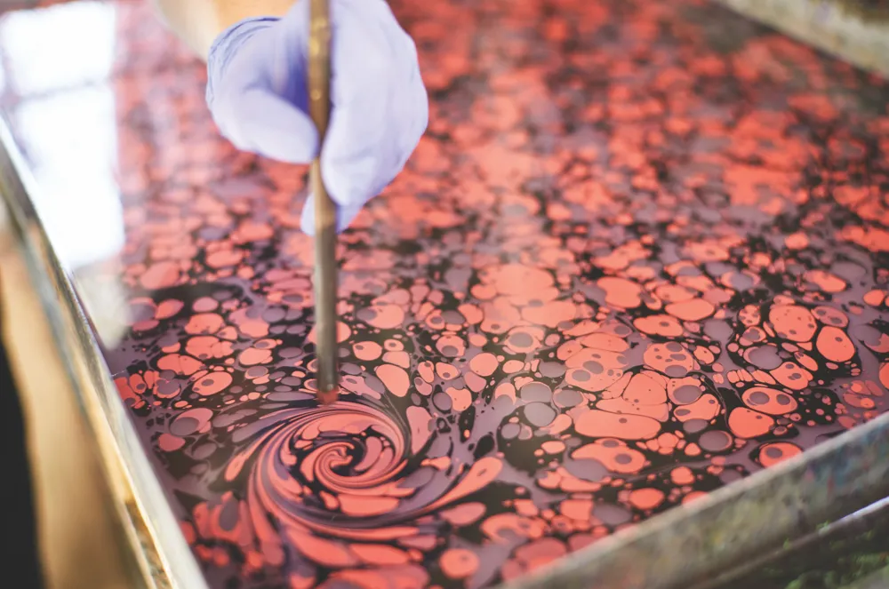 Jemma uses a stylus to swirl ink floating atop a tray of water