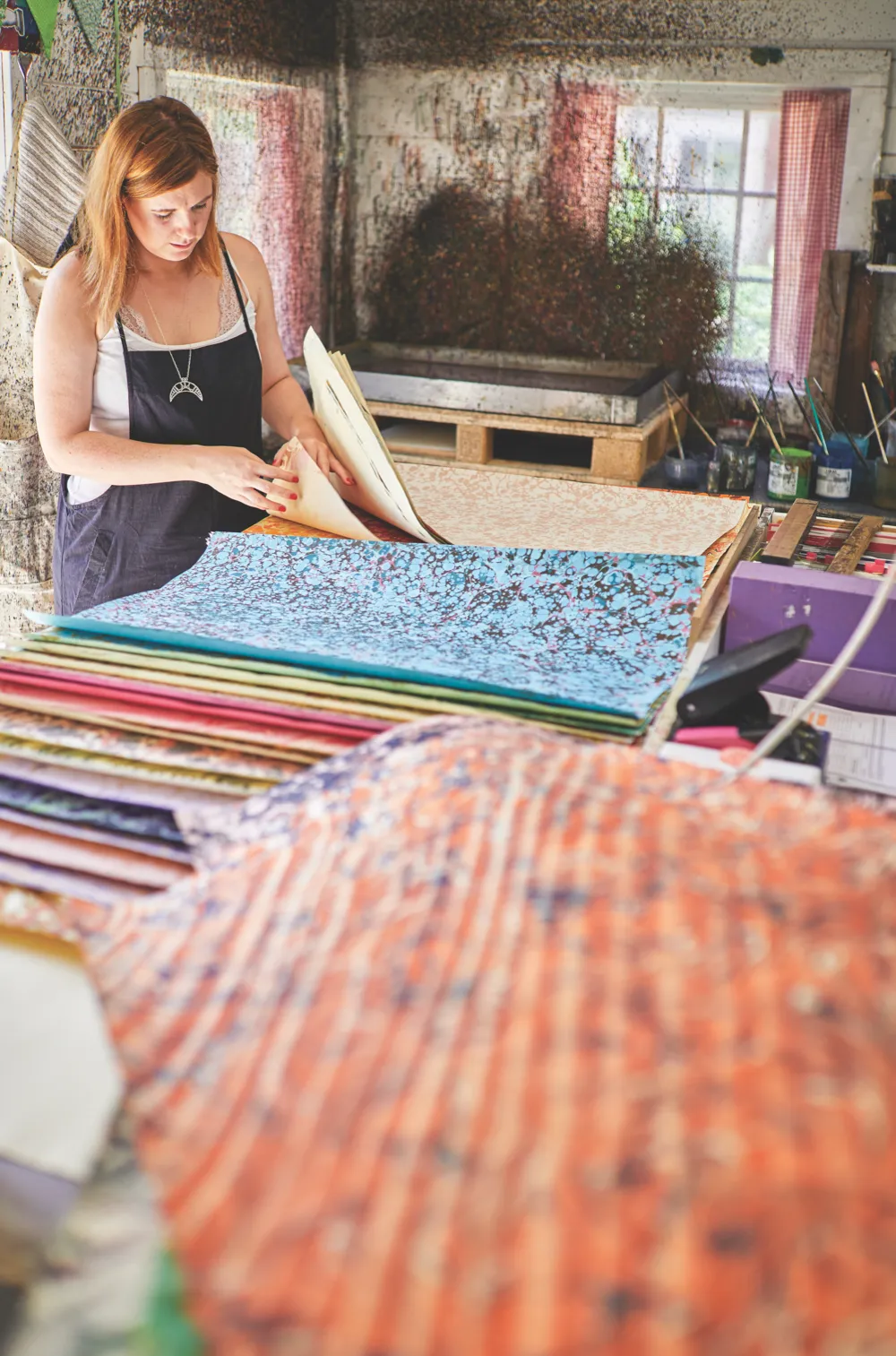 Jemma in her back garden workshop, surrounded by piles of richly marbled papers