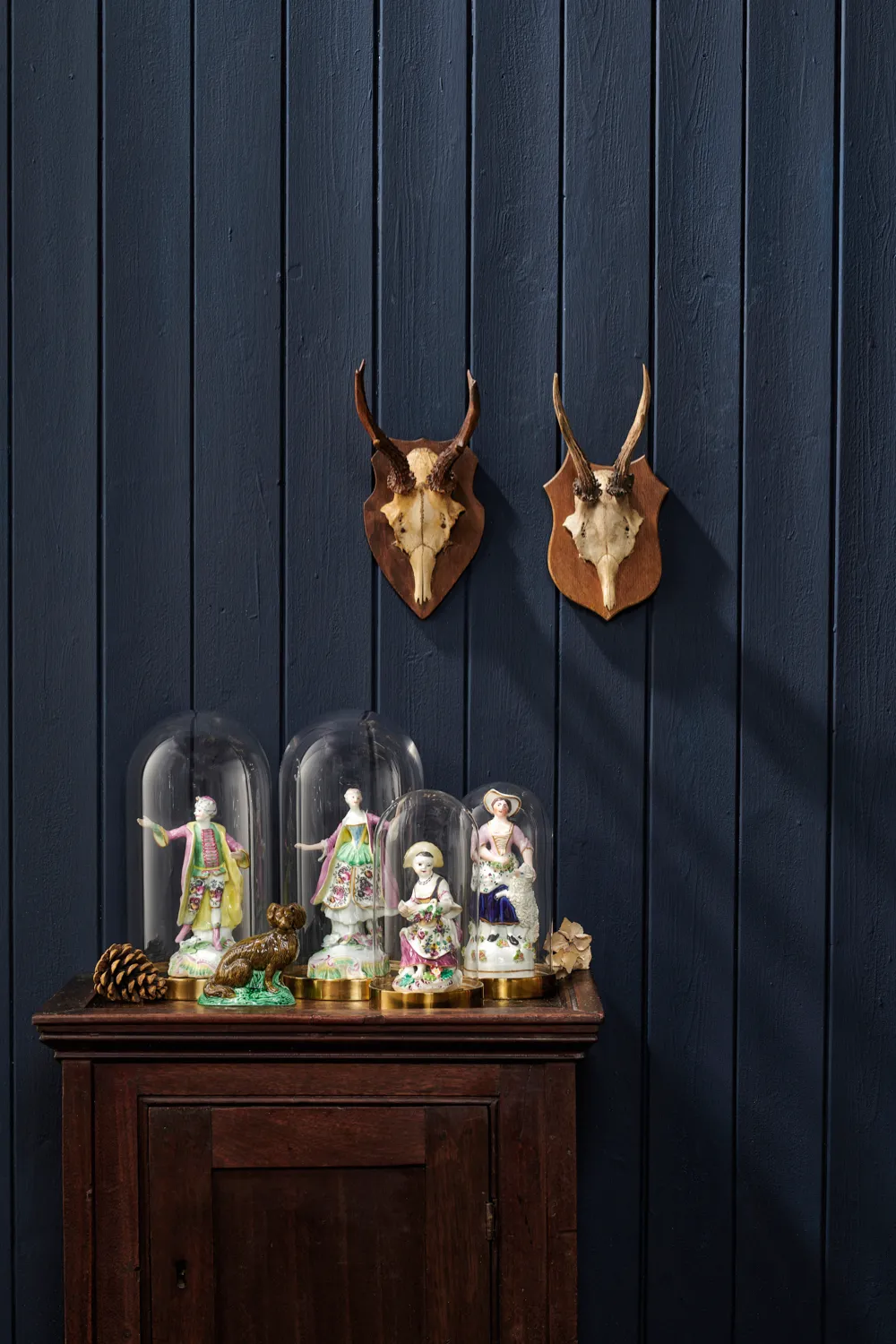 Figurines displayed in glass domes against a Farrow & Ball painted wall and antique mounted antlers