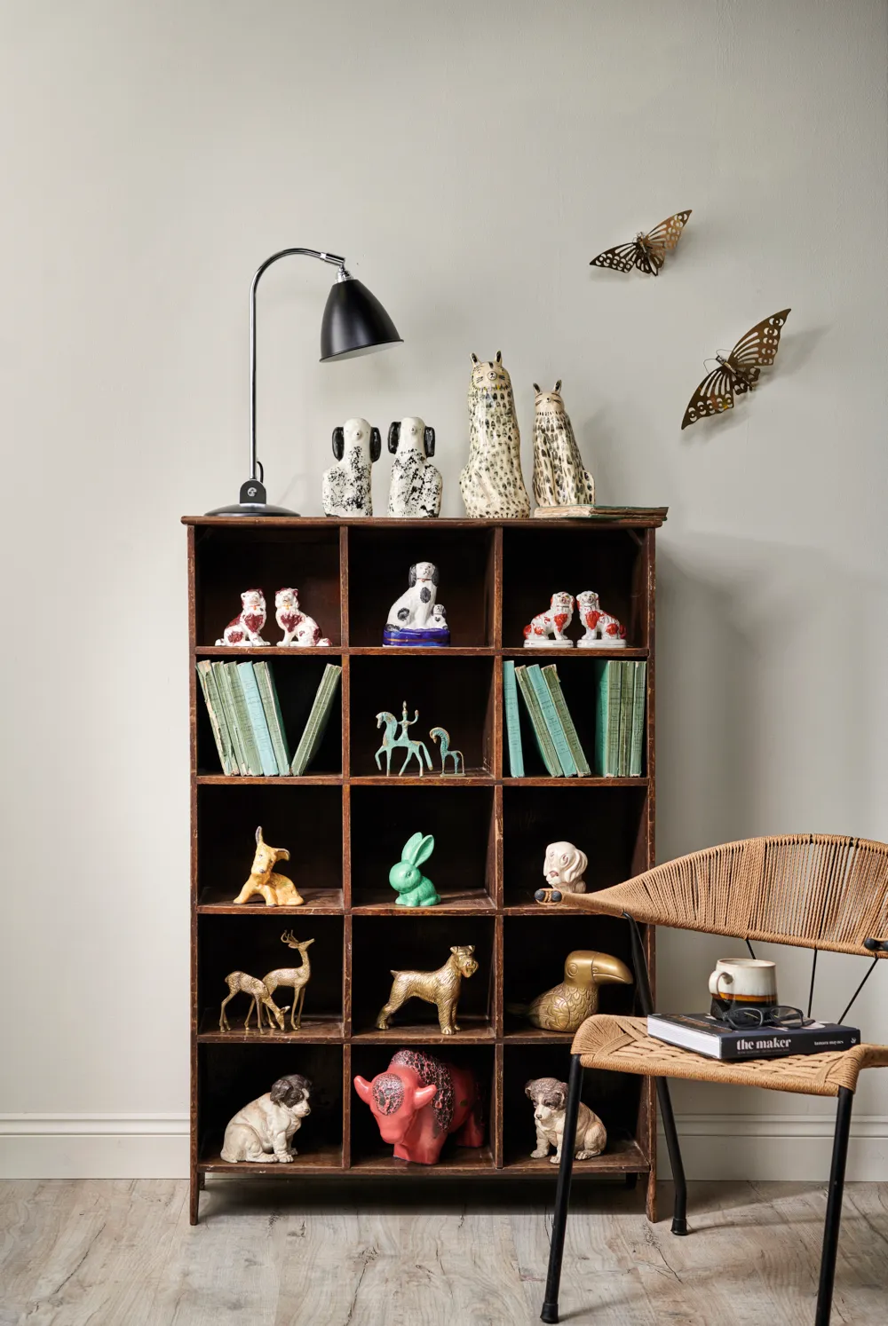 A colour co-ordinated display of miniatures in a pigeon hole unit with a Gubi lamp, vintage brass butterflies