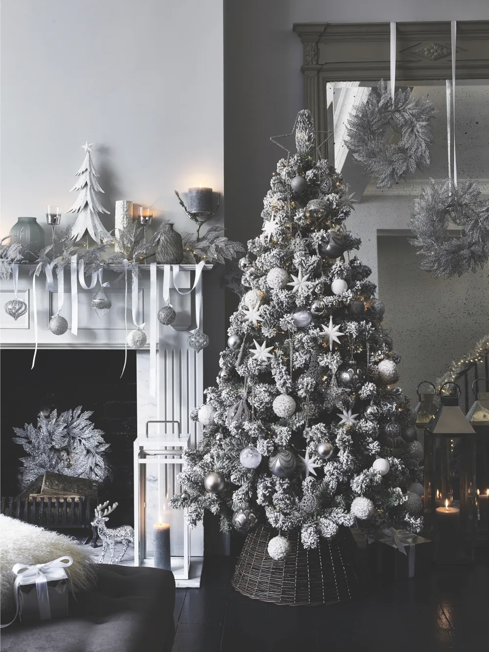 A white and silver hued tree sparkles next to a white fireplace with various white and silver decorations