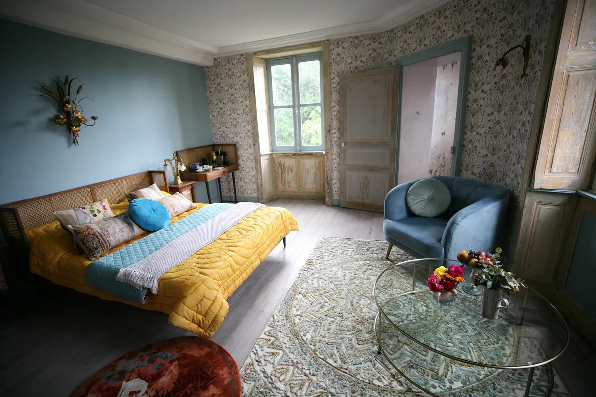 The Potagerie Suite in Chateau de la Motte Husson - a large room decorated in floral wallpaper with a wooden bed covered in a yellow bedspread