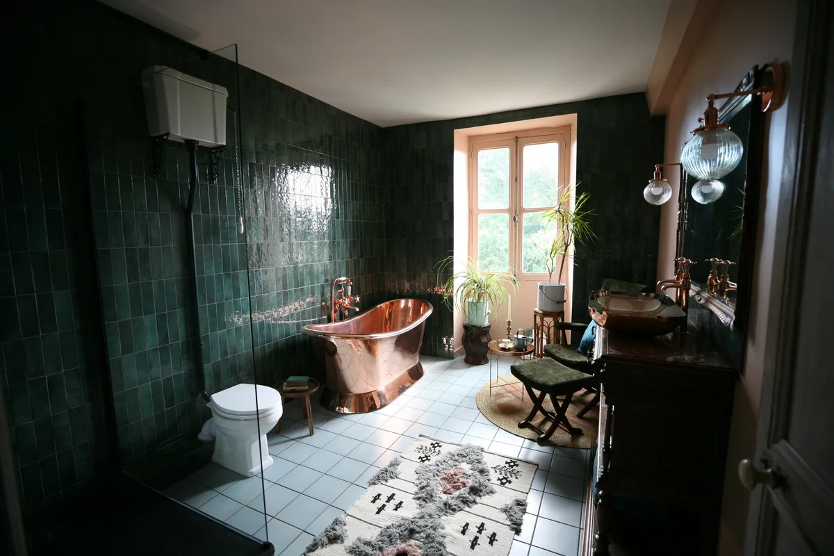 The Potagerie Suite bathroom at Chateau de la Motte Husson - walls are painted dark green and bold copper bathtub sits in the centre of the room