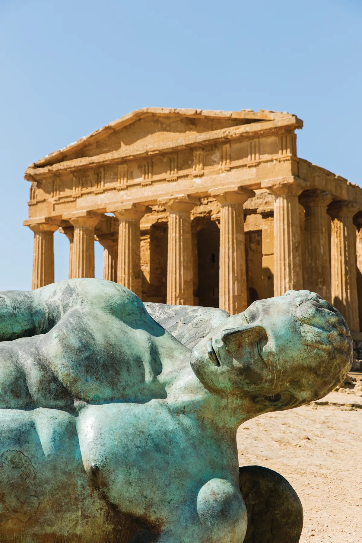 Bronze statue of Fallen Icarus resting in the foreground of a Greek Temple