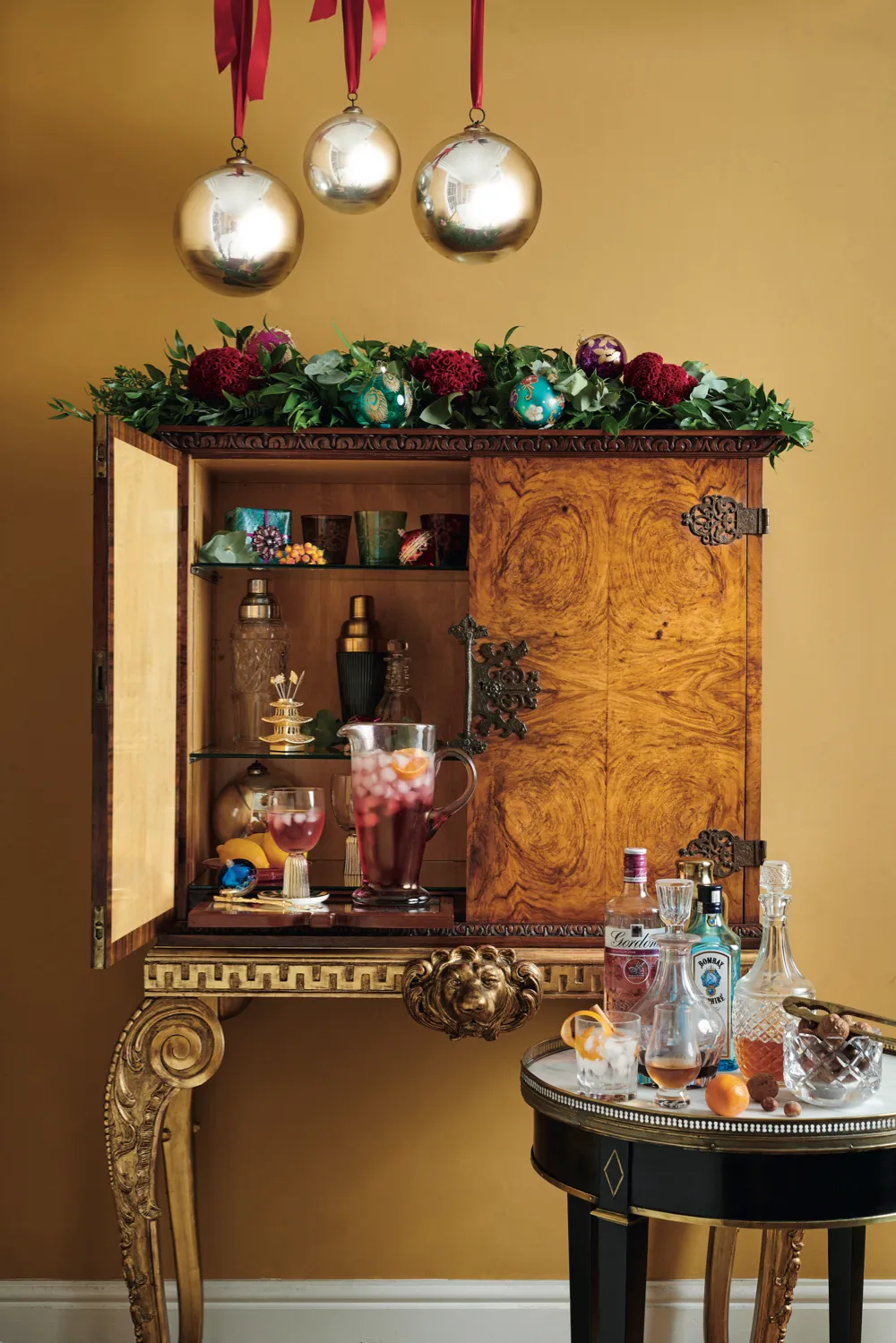 Drinks cabinet decorated with fresh greenery, a selection of artfully placed ornaments and a clutch of witch balls for a super-sized statement.