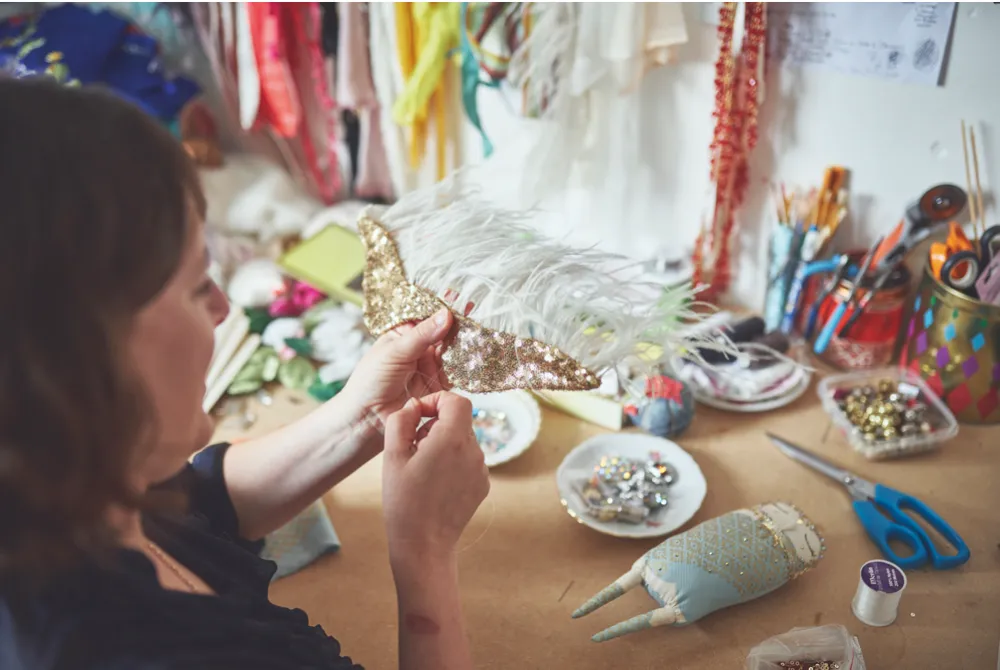Alice sewing gold sequins onto one of her enchanting doll designs