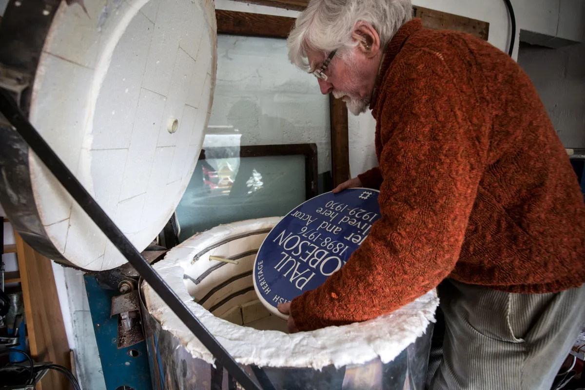 Frank Ashworth carefully lifts a freshly fired blue plaque out of the kiln.