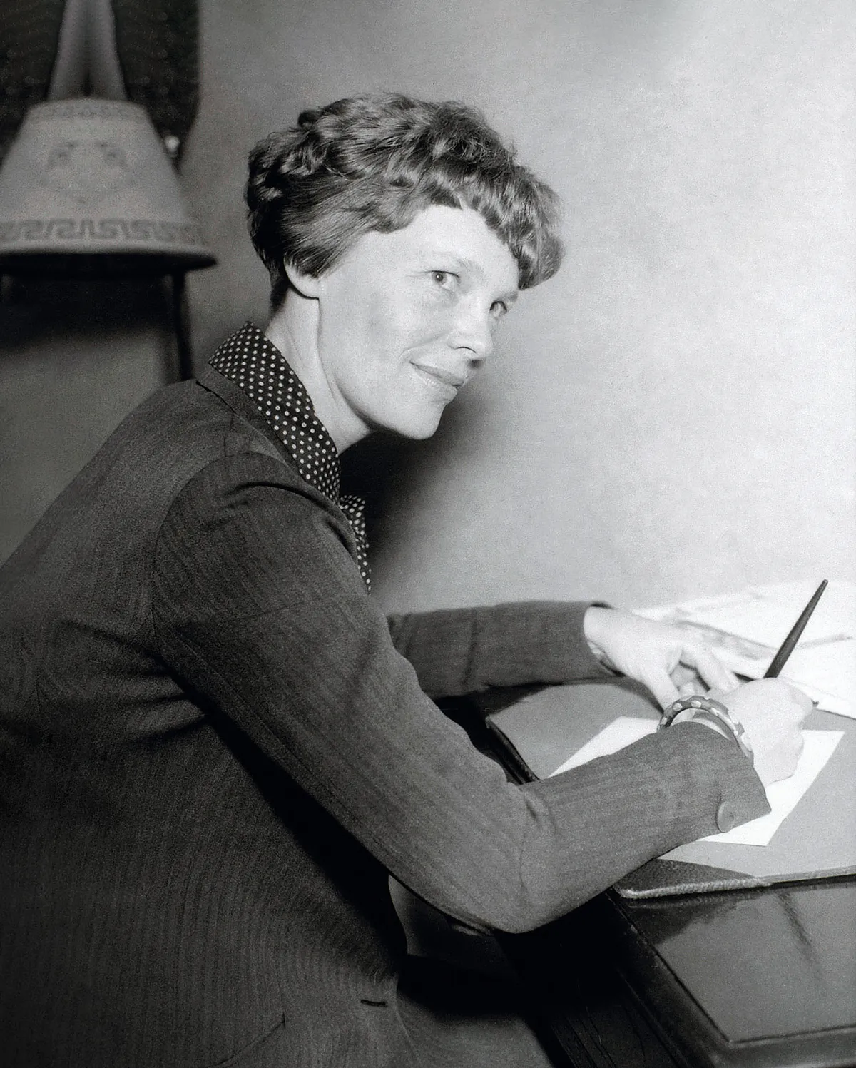 Una fotografía en blanco y negro de Amelia Earhart escribiendo en su escritorio.