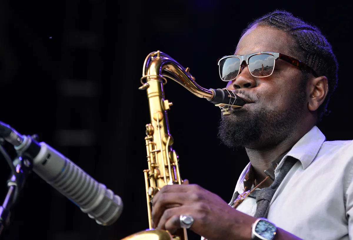 A photo of Soweto Kinch playing the saxophone in sunglasses