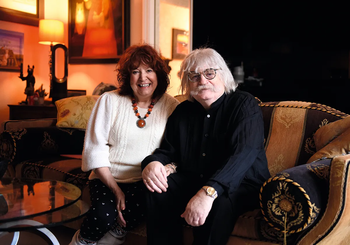 A photo of Karl Jenkins and his wife holding hands sitting on a sofa