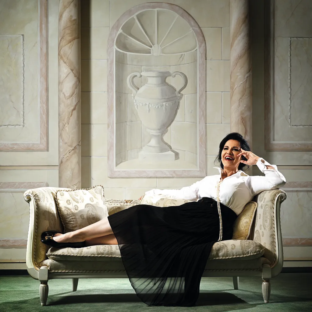 Angela Gheorghiu wears a white shirt and black skirt and sits on a chaise longue
