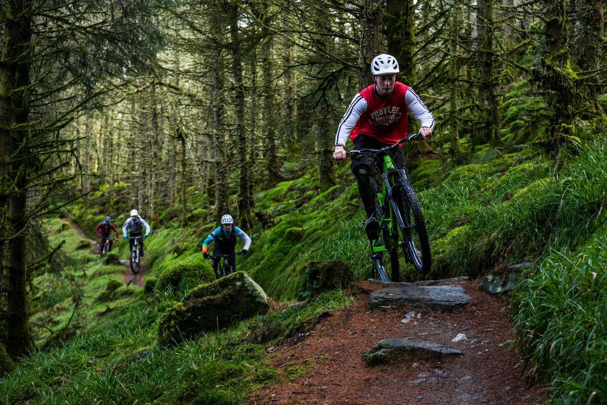 Leo Houseman leads out Ed Thomsett, Joe Breeden and Alex Evans on an MBUK Wrecking Crew photoshoot in Penmachno, North Wales. They're riding through a lush green forest.
