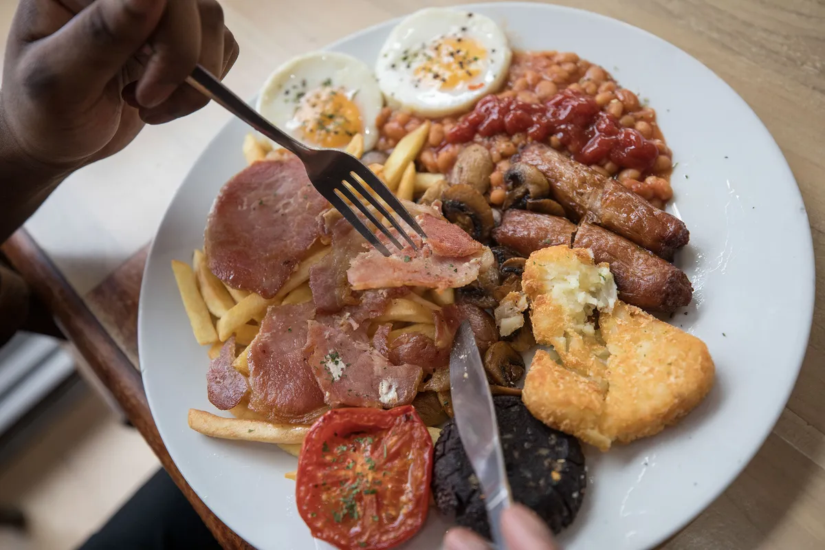 A customer eats the 'Super' full English breakfast at the 'Enough to Feed an Elephant' cafe in this arranged photograph in London, U.K., on Monday, July 10, 2017. British consumers could see the price of a fry-up -- a classic English breakfast with ingredients like bacon, sausages, orange juice, baked beans and mushrooms -- increase by almost 13 percent. Photographer: Simon Dawson/Bloomberg via Getty Images