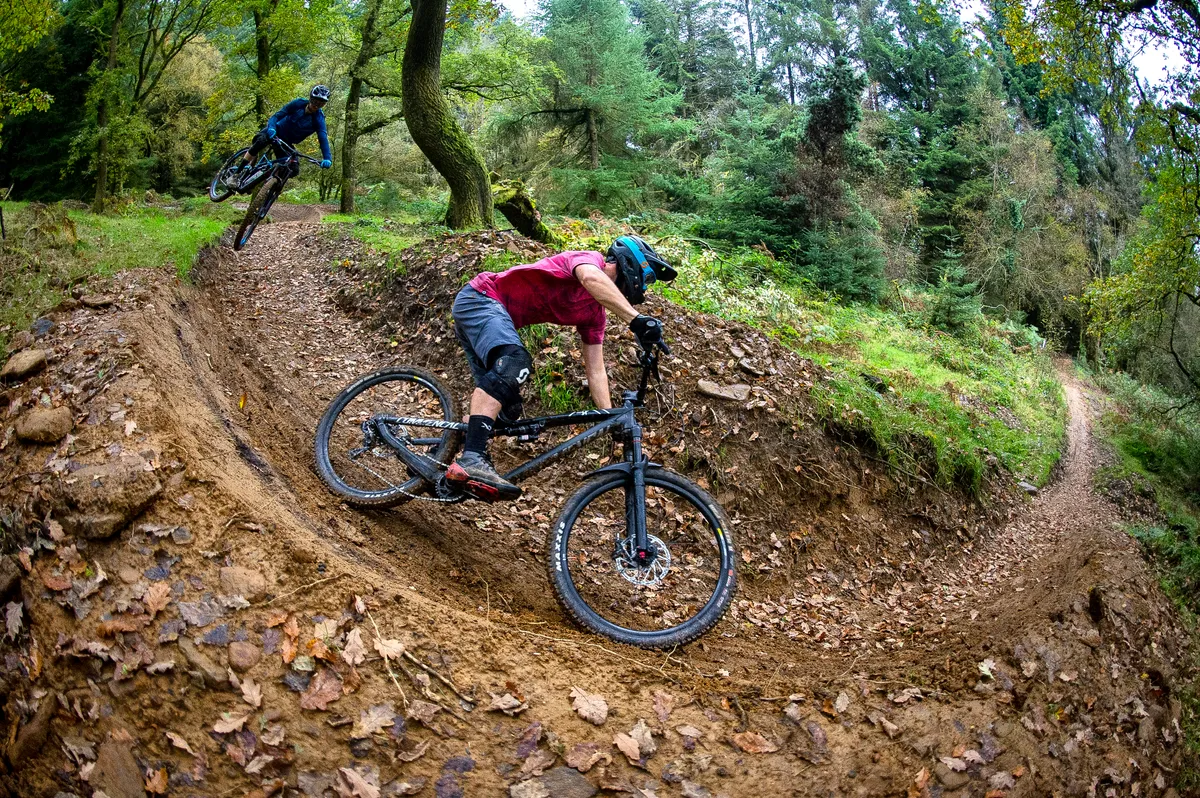 MBUK Staff members Alex Evans and Ed Thomsett ride a jump into a berm at BikePark Wales