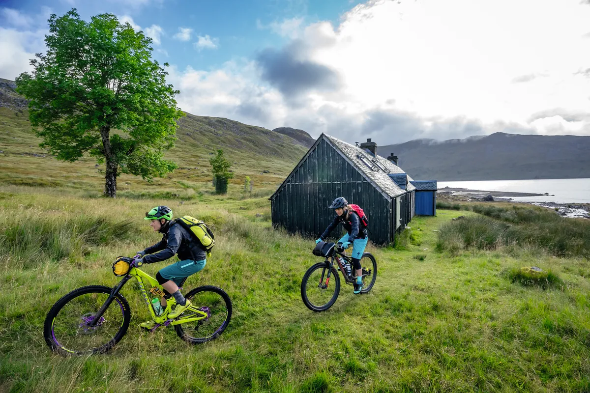 Rachael Walker and Hannah Barnes ride their bikes past a bothy in the Scottish Highlands