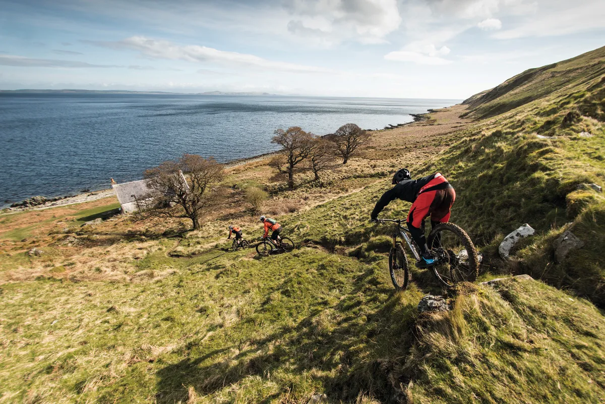 Riders head down to an abandoned cottage on the shoreline of Isle of Arran, Scotland