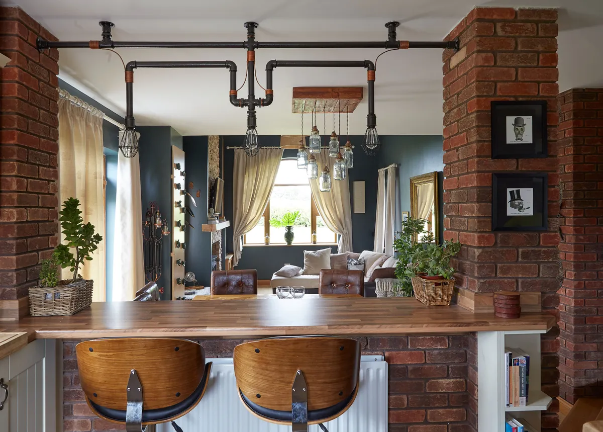 The breakfast bar overlooks the dining and living rooms, and serves as a divider to break up the open-plan space between them and the kitchen. Above it hangs one of the distinctive light fittings Shane has designed and built using plumbing parts