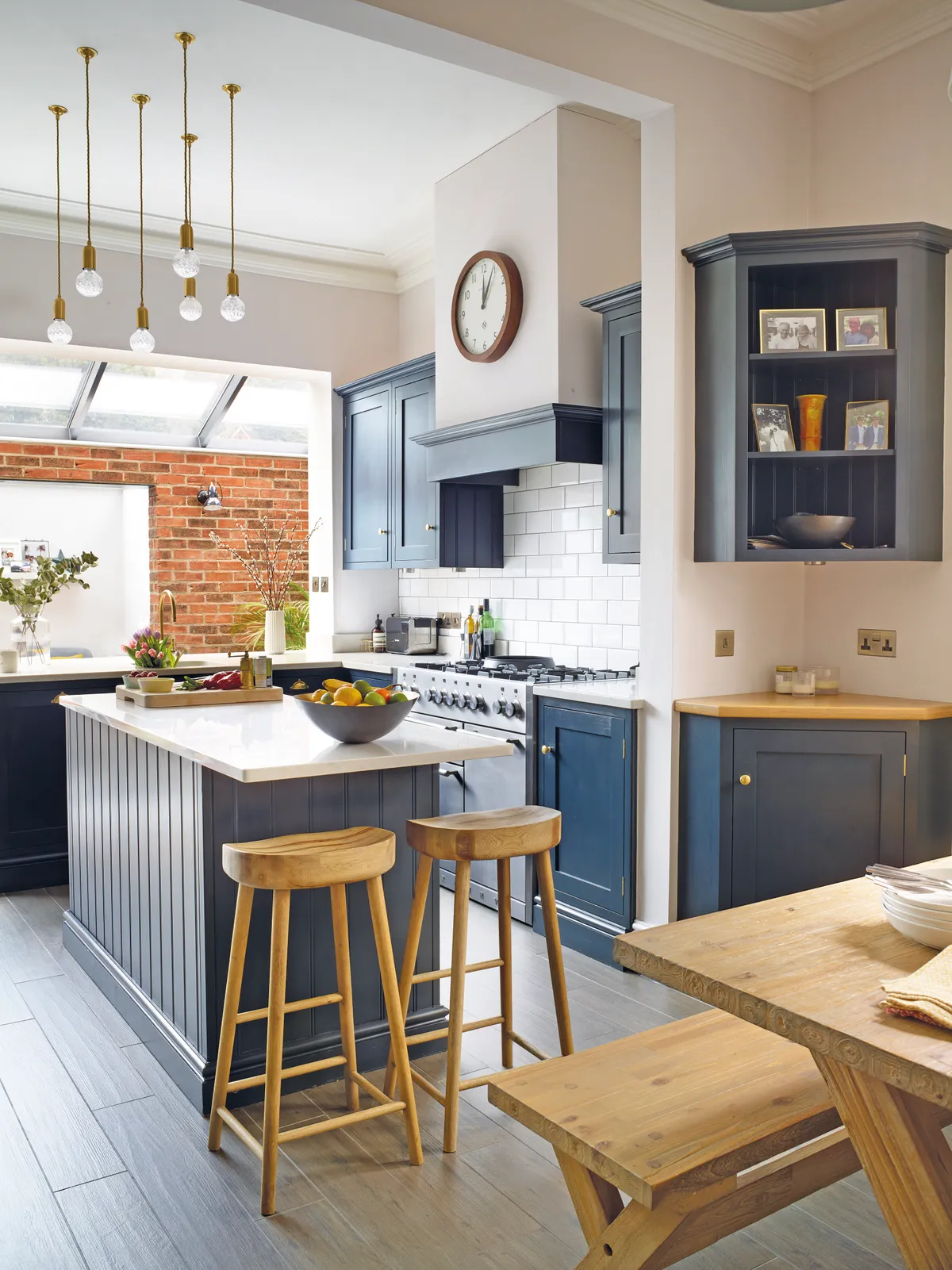 A row of skylights flood the kitchen with natural light, to make the space bright. Sarah ensures the sleek style remains homely by displaying family photographs in the open cabinetry. Wooden stools and a feature clock add a contemporary country feel