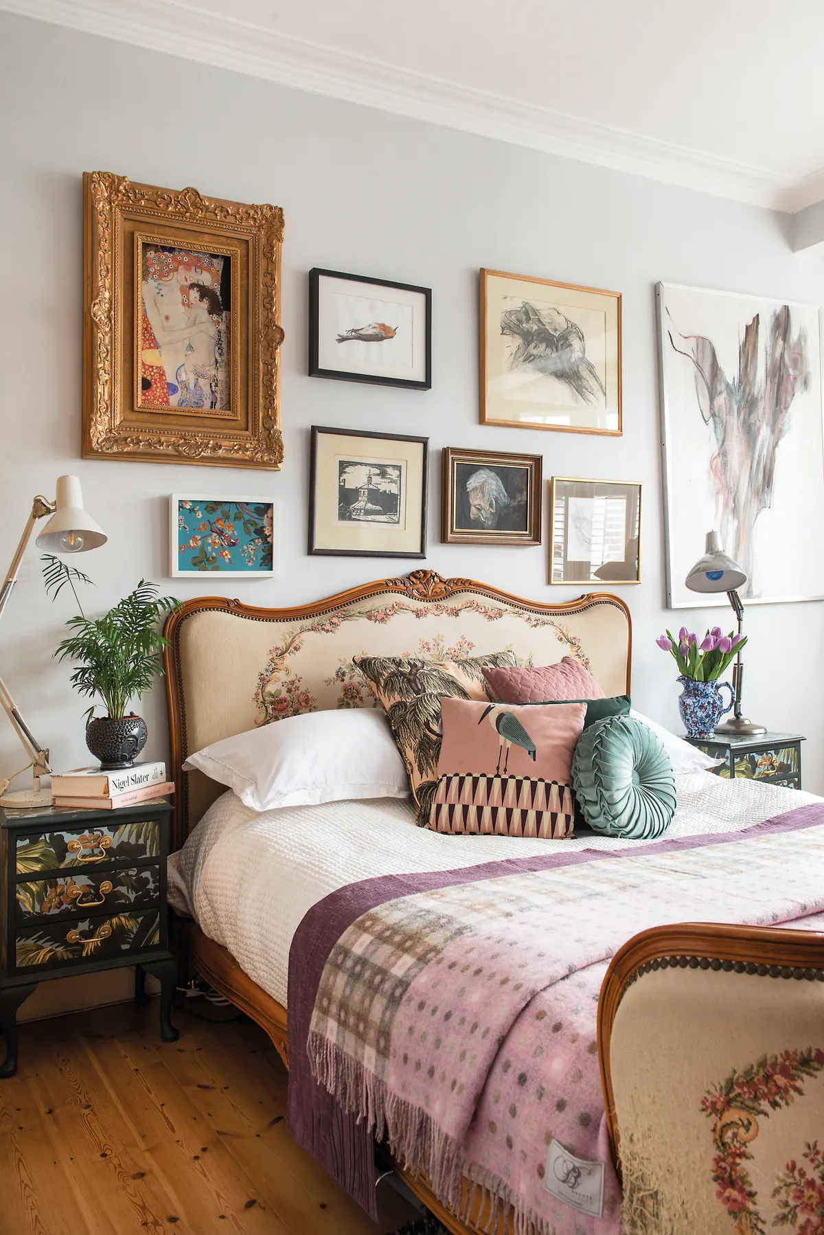 The bedroom walls are painted in Farrow & Ball’s Blackened, which acts as a subtle backdrop for the eclectic gallery wall. Vintage reading lamps add a contrasting functional feel beside the decorative upholstered bed