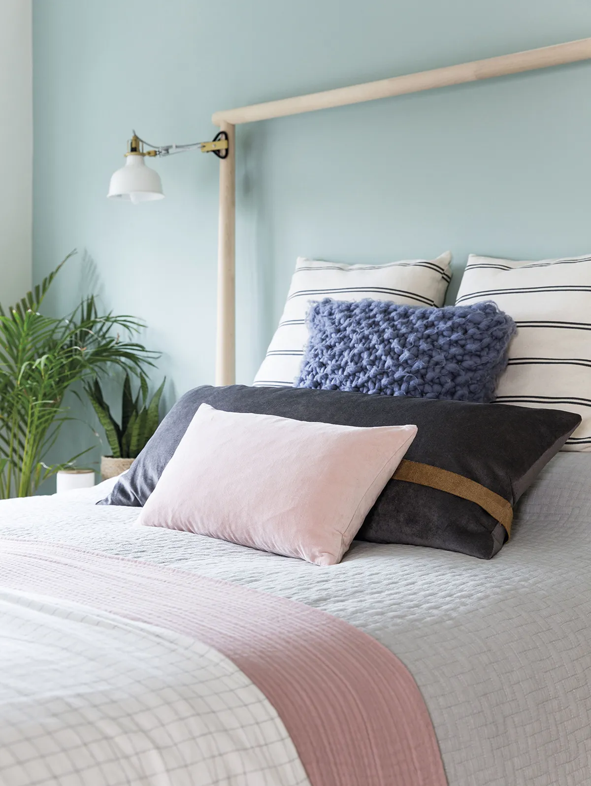 Layering up cushions, blankets and waffle bed linen in different tones and textures brings the bed to life, while a mix of fresh and faux plants helps to soften the space